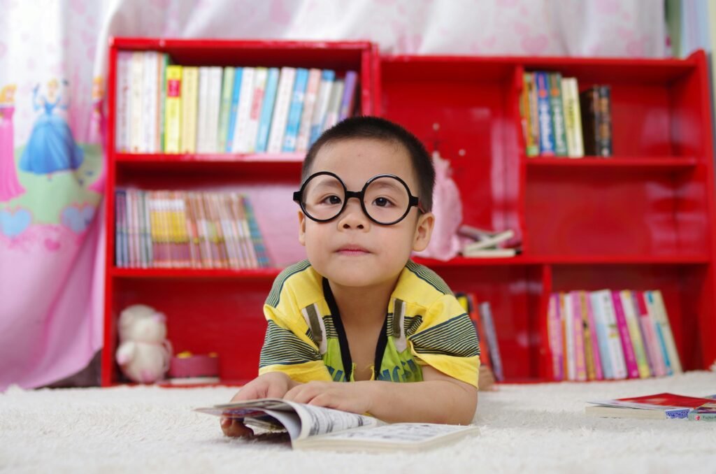 A cute child in glasses reading a book, surrounded by colorful shelves. Perfect shot of childhood learning indoors.