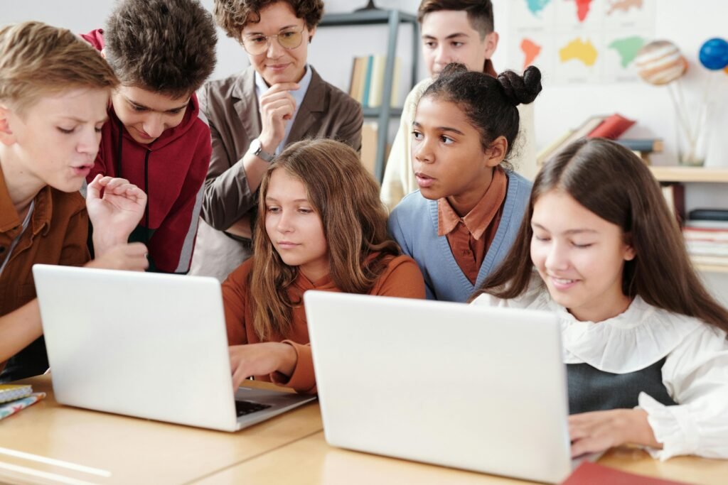 Teenage students actively collaborate on laptops in an educational environment with guidance from a teacher.